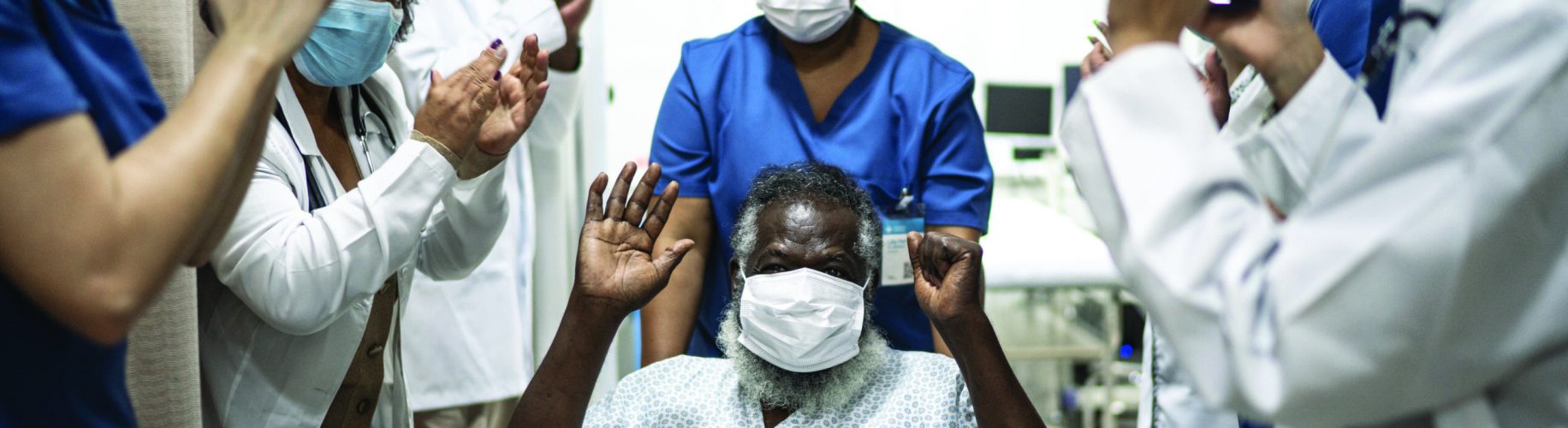 Doctors and nurses celebrating senior man leaving the hospital after recovery - wearing protective face mask